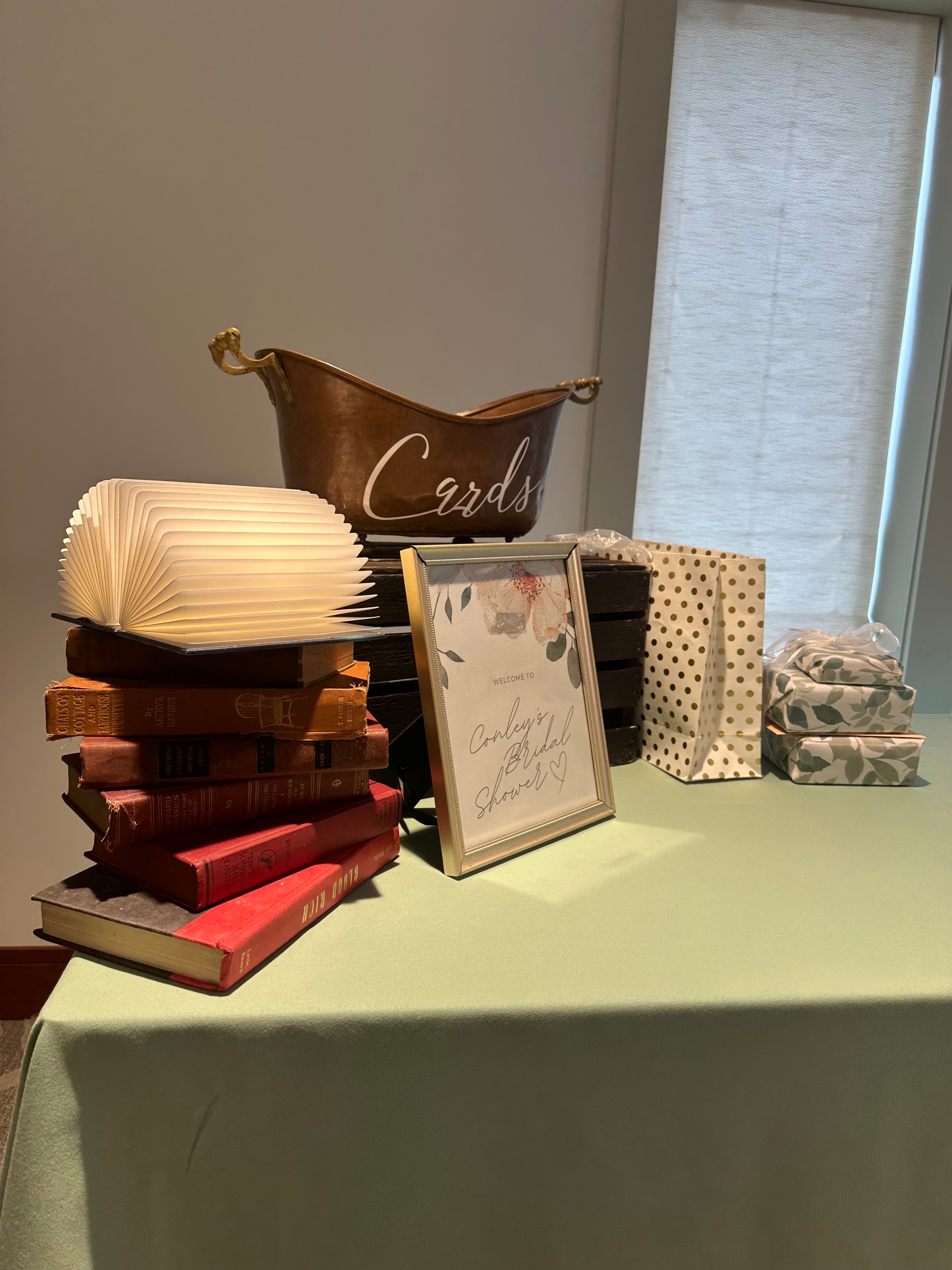 Bridal shower welcome table with cards box, framed sign, book light, and vintage books
