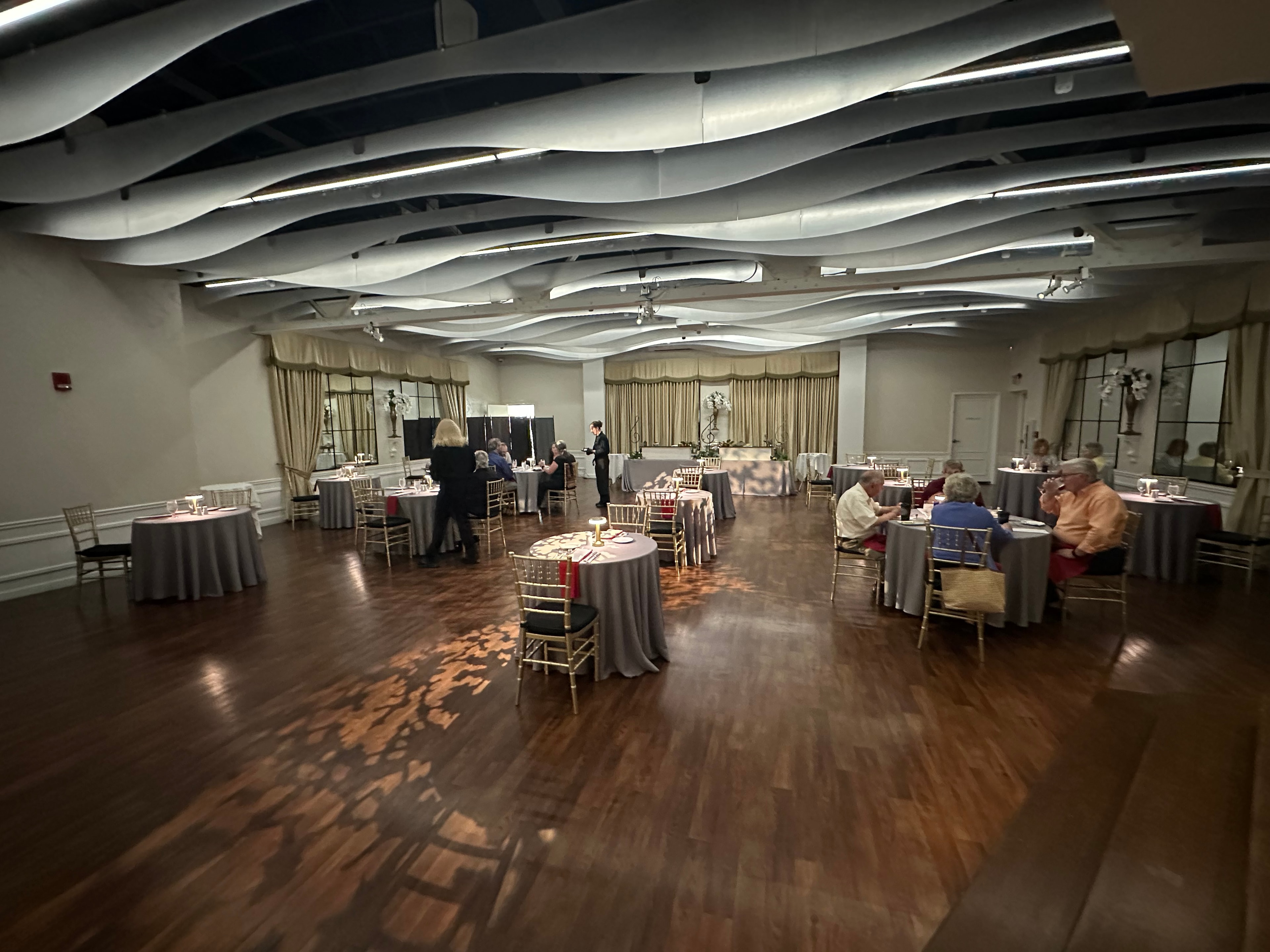Corporate dinner event in a ballroom with wave ceiling, round tables, and gold chiavari chairs