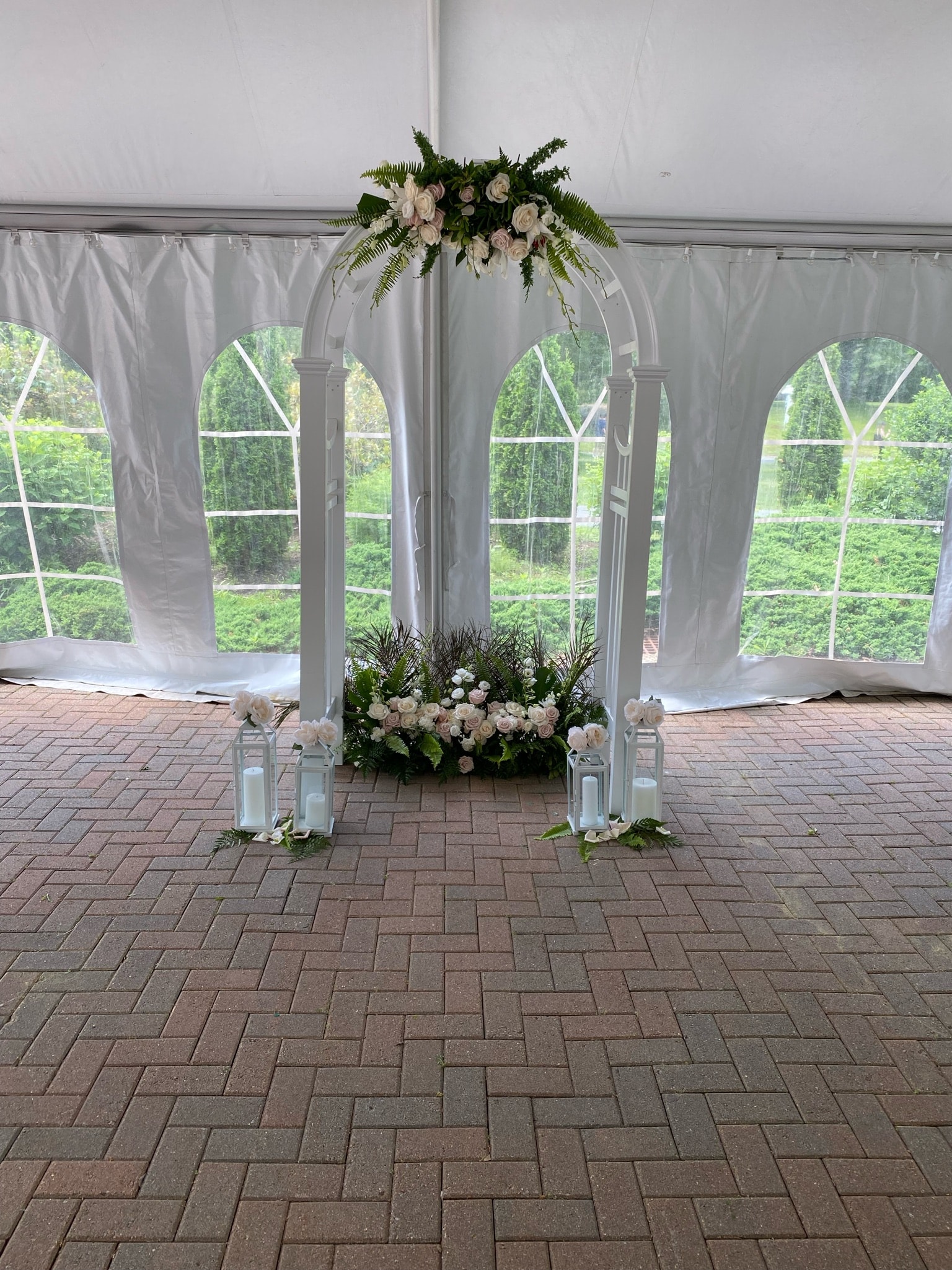 White wedding ceremony arch with roses and ferns inside a tent at The Flint's wedding