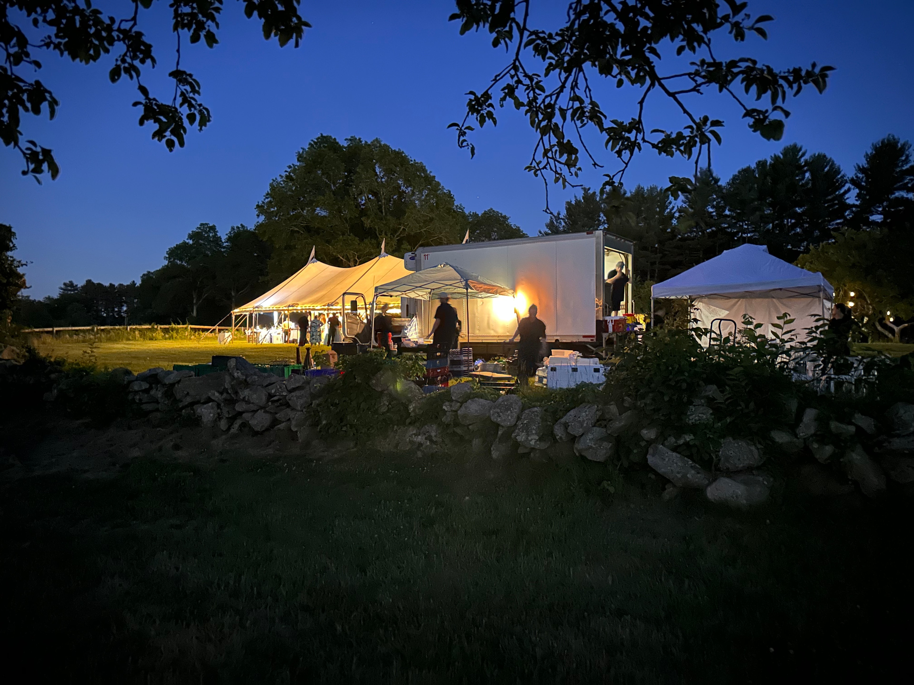 Illuminated wedding tents at dusk with staff working behind the scenes